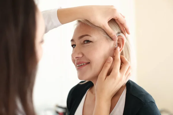 Otorinolaringoiatra mettere l'apparecchio acustico nell'orecchio della donna su sfondo chiaro — Foto Stock