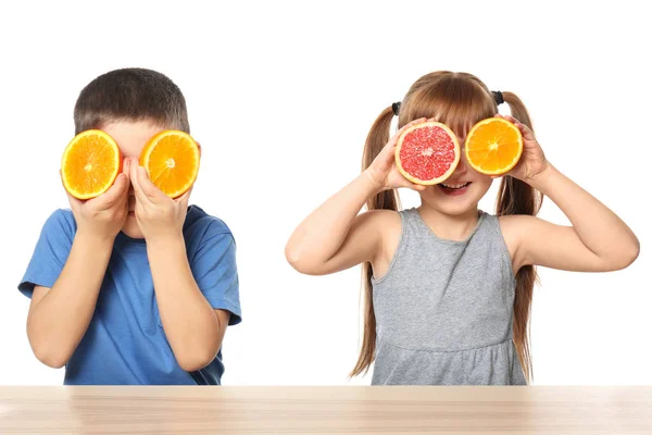 Aranyos kis gyermekek citrusfélék asztalnál fehér háttér — Stock Fotó