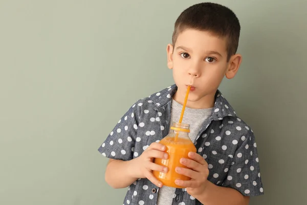 Funny little boy drinking citrus juice on color background — Stock Photo, Image