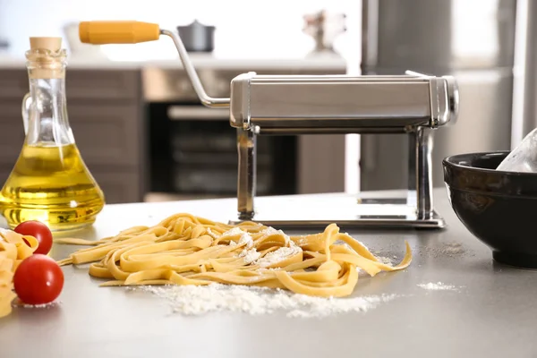 Kovové těstoviny maker a nevařené nudle na kuchyňském stole — Stock fotografie