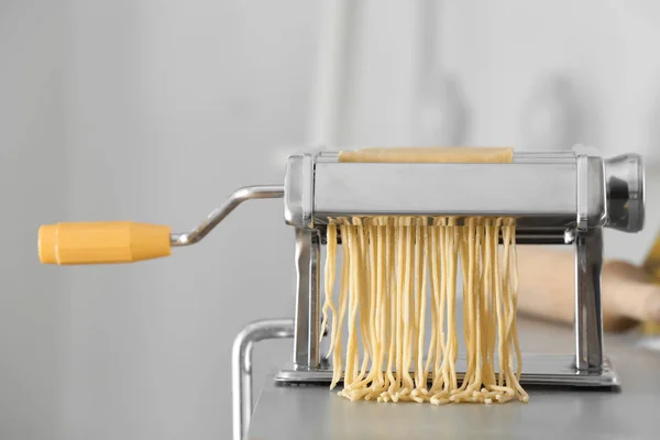 Metal pasta maker with dough on table against blurred background — Stock Photo, Image
