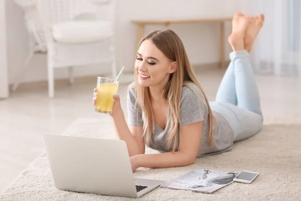 Beautiful young woman drinking citrus juice while working with laptop at home — Stock Photo, Image