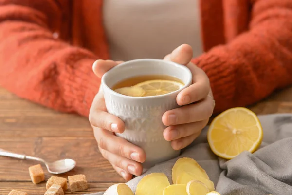 Woman holding cup of tea with lemon and ginger on wooden table — Stock Photo, Image