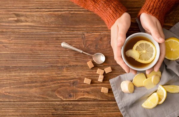 Woman holding cup of tea with lemon and ginger on wooden table — Stock Photo, Image