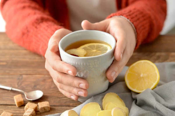 Woman holding cup of tea with lemon and ginger on wooden table — Stock Photo, Image