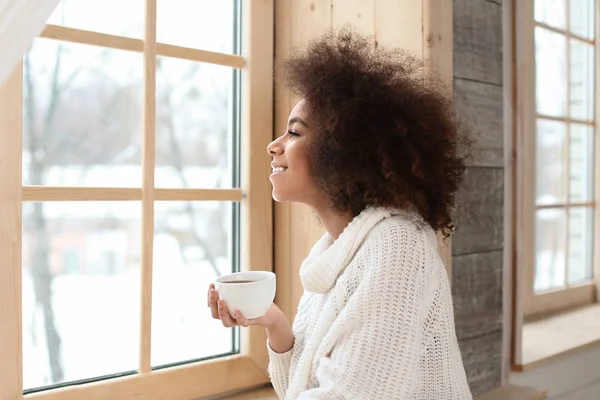 Beautiful African-American woman drinking tea near window — Stock Photo, Image