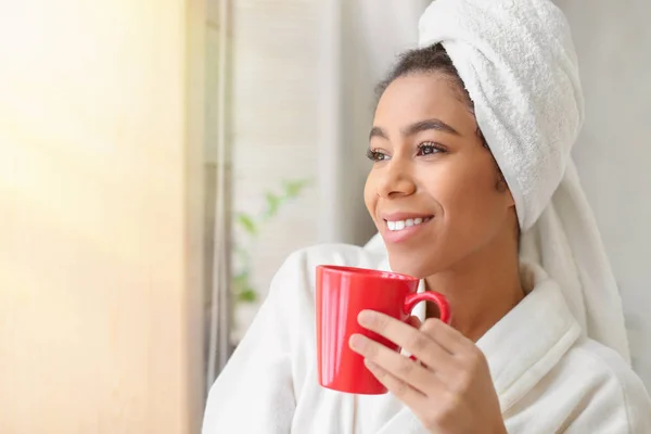 Beautiful African-American woman in bathrobe drinking tea at home — Stock Photo, Image