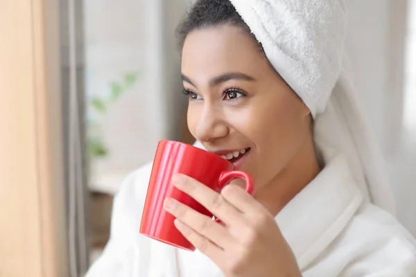 Hermosa mujer afroamericana en albornoz bebiendo té en casa — Foto de Stock