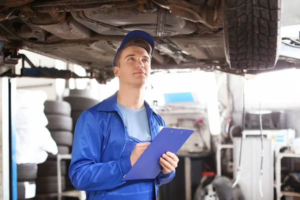 Male mechanic with clipboard examining car in service center — Stock Photo, Image