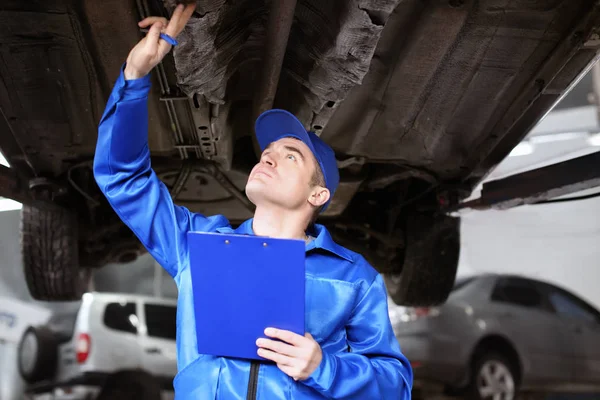 Mecánico masculino con portapapeles examinando el coche en el centro de servicio — Foto de Stock