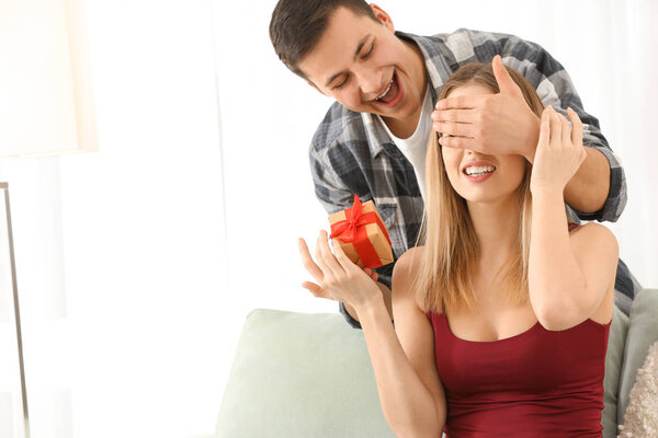 Молодой человек дарит подарок своей любимой девушке дома

