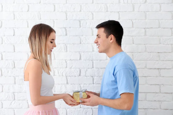 Happy young couple with gift box near white brick wall — Stock Photo, Image