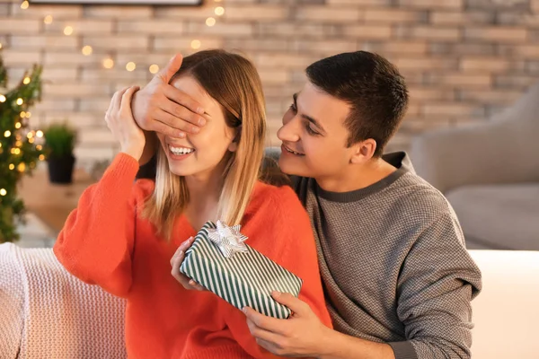 Young man giving Christmas present to his beloved girlfriend at home — Stock Photo, Image