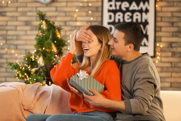 Young man giving Christmas present to his beloved girlfriend at home