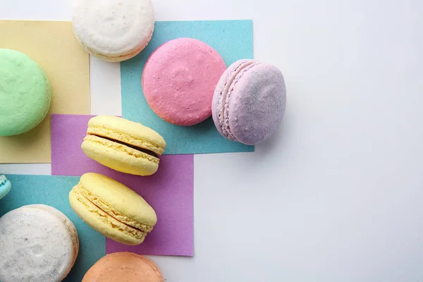 Tasty colorful macarons with sheets of paper on white background — Stock Photo, Image