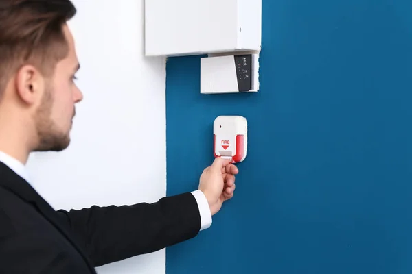 Young man pulling handle of fire alarm station, indoors — Stock Photo, Image