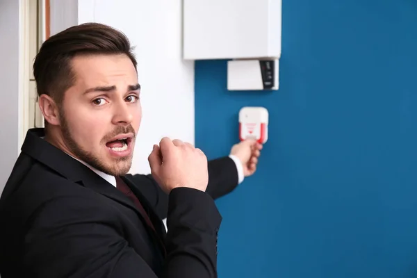 Young man pulling handle of fire alarm station, indoors