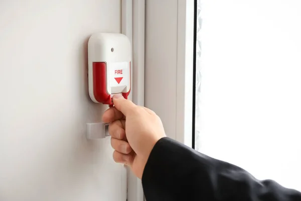 Young man pulling handle of fire alarm station, indoors — Stock Photo, Image