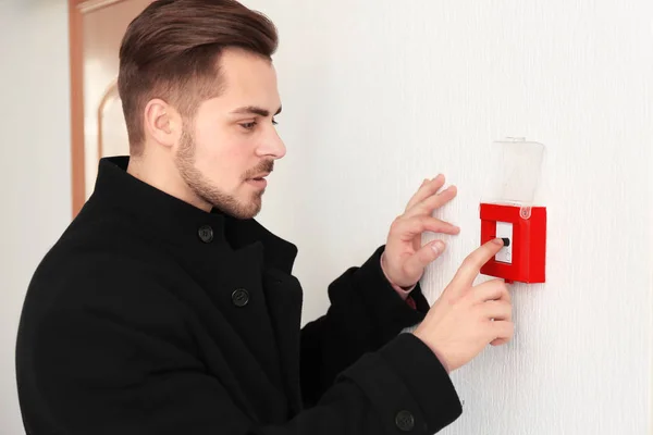 Young man pushing button of fire alarm system, indoors — Stock Photo, Image