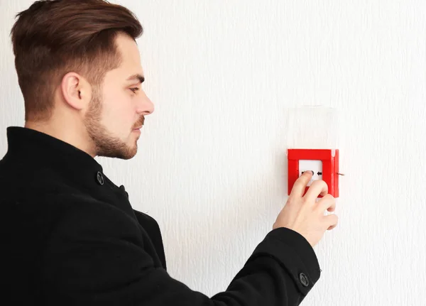 Young man pushing button of fire alarm system, indoors — Stock Photo, Image