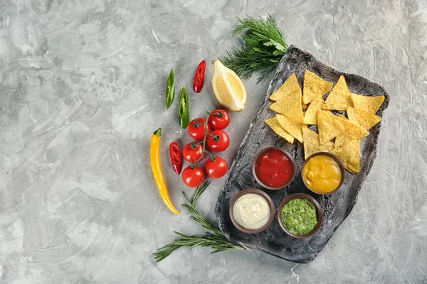 Composition avec différentes sauces et nachos sur fond gris texturé, vue de dessus — Photo