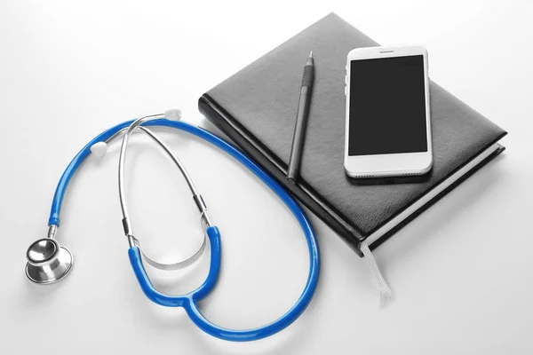 Stethoscope with smartphone and notebook on white background — Stock Photo, Image