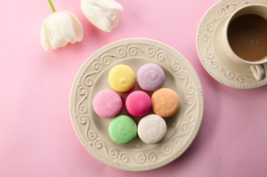 Plaka ile lezzetli macarons, fincan kahve ve çiçek renk arka plan, üstten görünüm