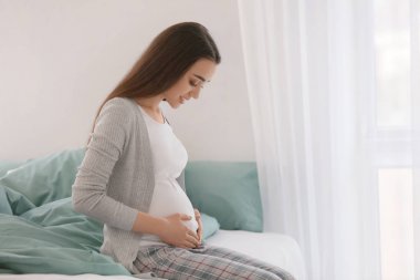 Sabah yatağın üstüne oturan güzel hamile kadın