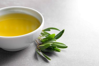 Zeytinyağı ve gri arka plan üzerinde yeşil yaprakları ile kase