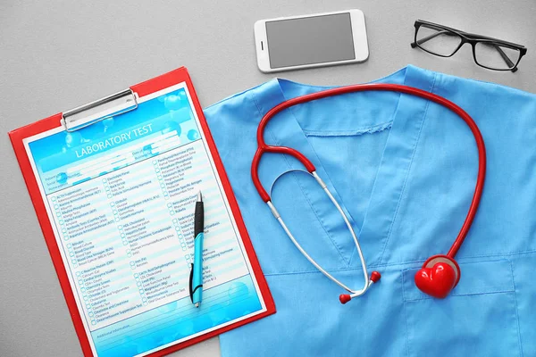 Estetoscópio com telefone, teste de laboratório e uniforme médico azul na mesa — Fotografia de Stock