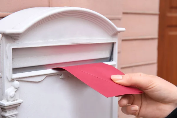 Жінка кладе конверт у поштову скриньку на стіні будівлі на відкритому повітрі — стокове фото