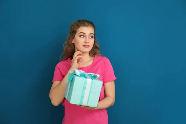 Beautiful young woman with gift box on color background — Stock Photo, Image