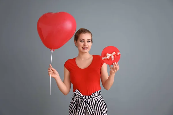 Mulher bonita com caixa de presente e balão em forma de coração no fundo de cor — Fotografia de Stock