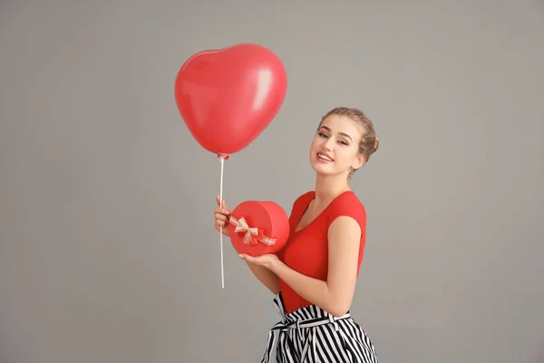 Hermosa mujer joven con caja de regalo y globo en forma de corazón sobre fondo de color — Foto de Stock