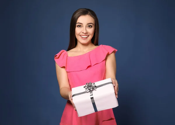 Beautiful young woman with gift box on color background — Stock Photo, Image