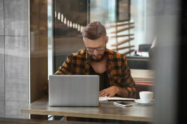 Молодий фрілансер з ноутбуком, що працює в кафе — стокове фото