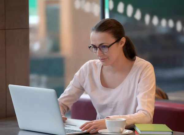 Junge Freiberuflerin mit Laptop arbeitet im Café — Stockfoto