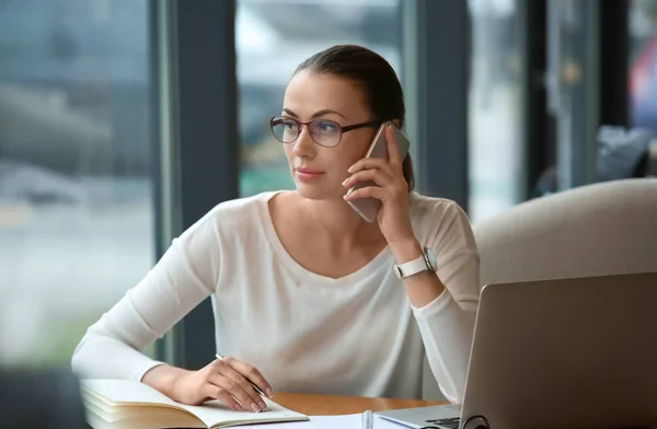 Young freelancer with mobile phone and laptop working in cafe — Stock Photo, Image