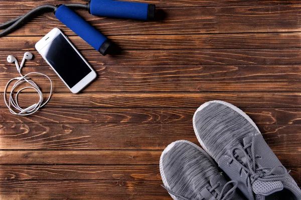 Composición plana con zapatillas, smartphone y cuerda de salto sobre fondo de madera. Entrenamiento en el gimnasio — Foto de Stock