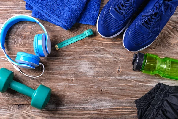 Composición plana con zapatillas, auriculares, mancuerna y botella de agua sobre fondo de madera. Entrenamiento en el gimnasio — Foto de Stock