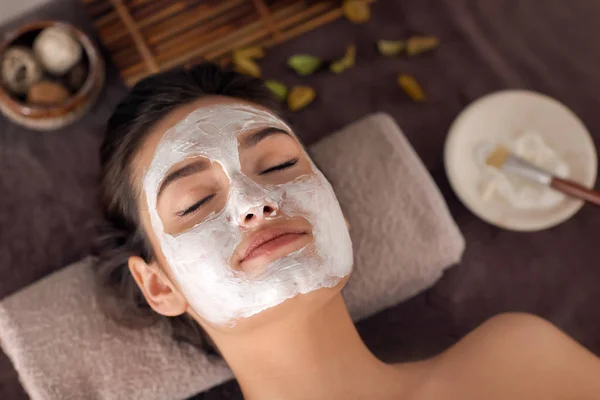 Jovem com máscara facial relaxante na mesa de massagem no salão de spa — Fotografia de Stock