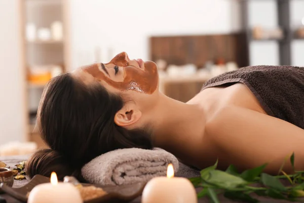 Junge Frau mit Gesichtsmaske entspannt auf Massagetisch im Wellness-Salon — Stockfoto
