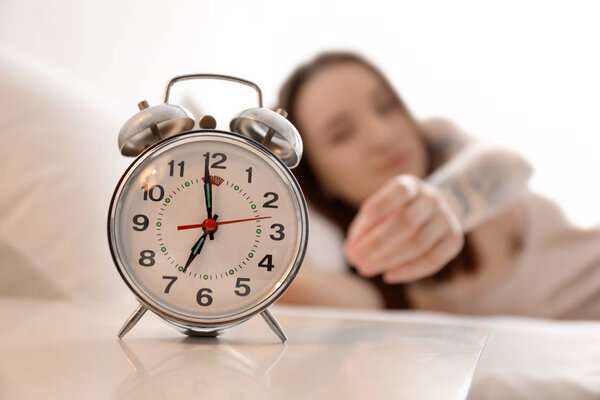Young woman reaching for alarm clock in bed. Early morning