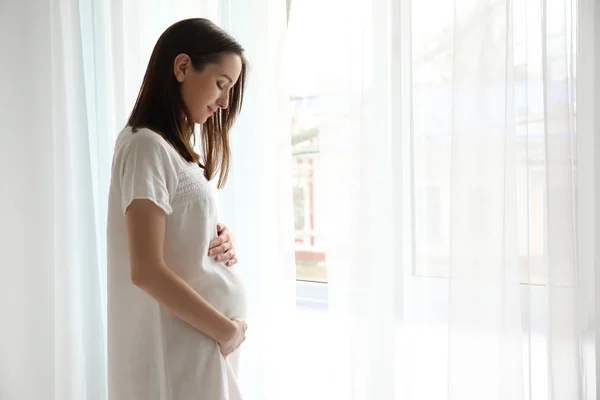 Beautiful pregnant woman standing near window in morning — Stock Photo, Image