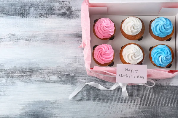 Cupcakes saborosos em caixa e cartão com palavras DIA DA MÃE DE AVALIAÇÃO na mesa — Fotografia de Stock