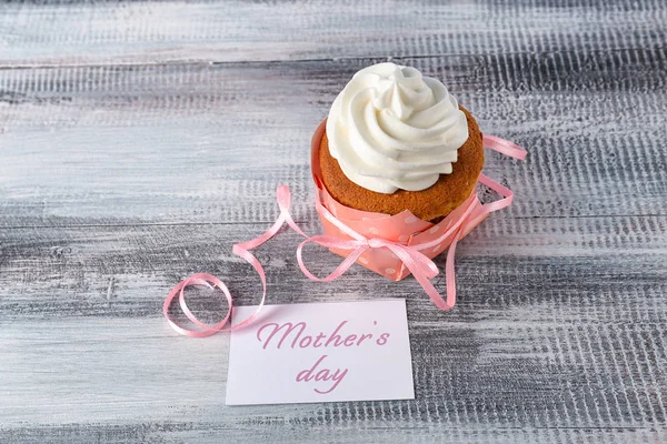 Tasty cupcake and card with words MOTHER'S DAY on wooden background — Stock Photo, Image