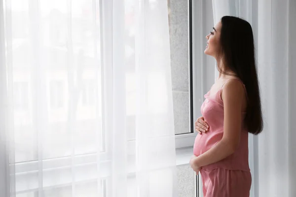 Krásná těhotná žena stojící u okna v ranní — Stock fotografie