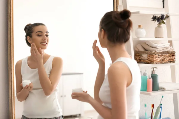 Mujer embarazada joven aplicando crema facial en la mañana — Foto de Stock