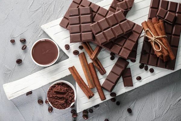 Composition plate avec chocolat savoureux, grains de café et bâtonnets de cannelle sur planche de bois — Photo