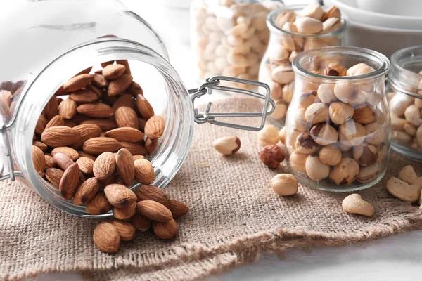 Overturned glass jars with different nuts on table — Stock Photo, Image